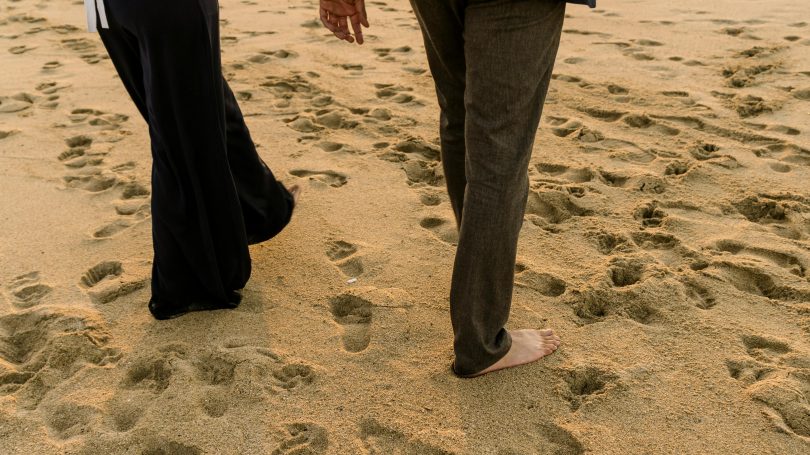 Close-up of a couple walking barefoot on a sandy beach, leaving footprints behind, symbolizing the journey of secondary infertility and personal reflection.