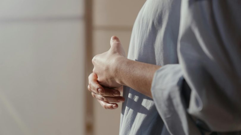 A person in a light blue shirt clasping their hands in front of them.