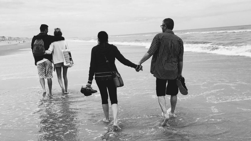 Two couples walking along the beach, holding hands, representing emotional support and relationships.