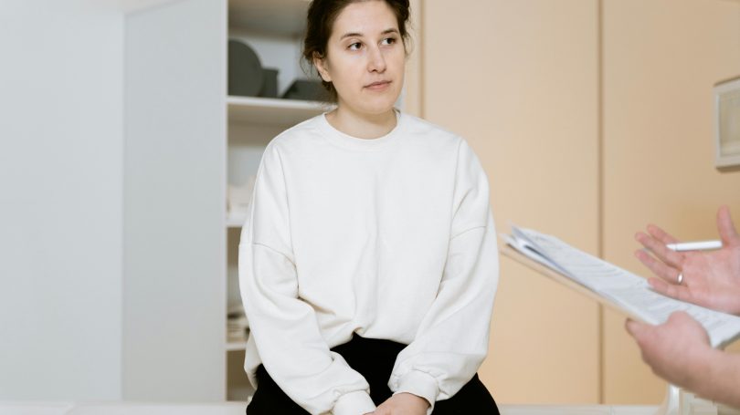 A woman sitting on a medical examination table, attentively listening to a healthcare professional during a consultation.