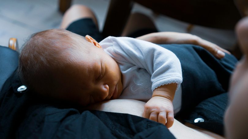 Newborn baby sleeping on parent's chest, skin-to-skin contact for bonding and breastfeeding support.