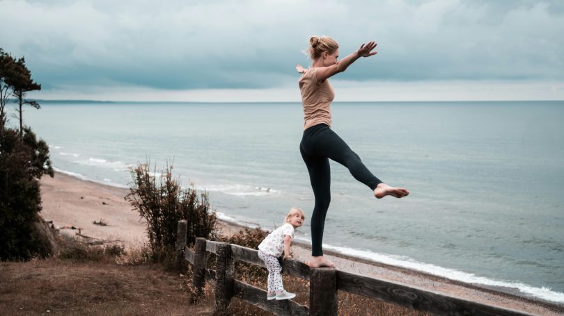 Woman balancing on a beam in nature next to her child