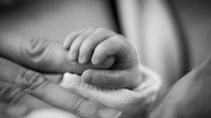A newborn baby’s tiny hand gently grasping an adult’s finger, symbolizing connection and care.