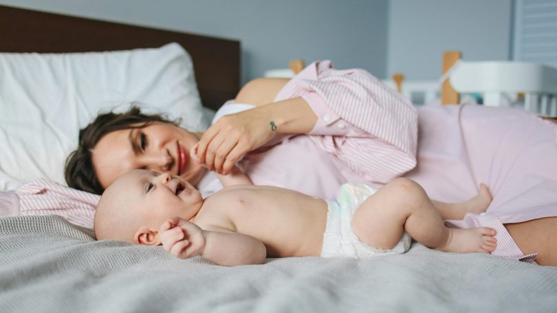 A mother lying on the bed with her baby, gently interacting and bonding, representing postpartum emotions and baby blues.