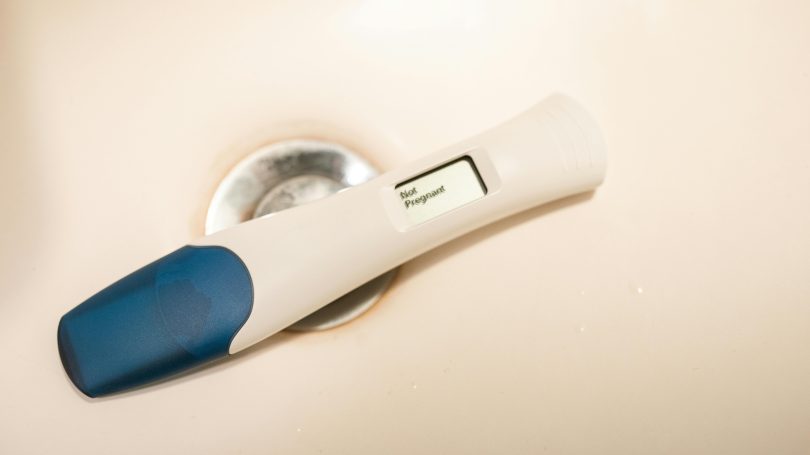 A digital pregnancy test displaying a positive result, placed on a bathroom sink.
