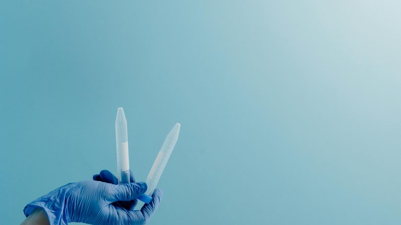A gloved hand holds two test tubes against a blue background