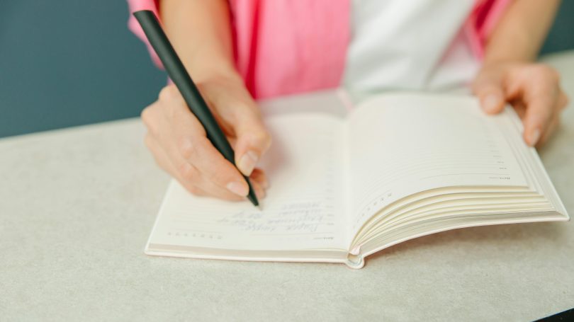 A woman writing in a fertility tracking journal, recording her menstrual cycle for natural fertility awareness