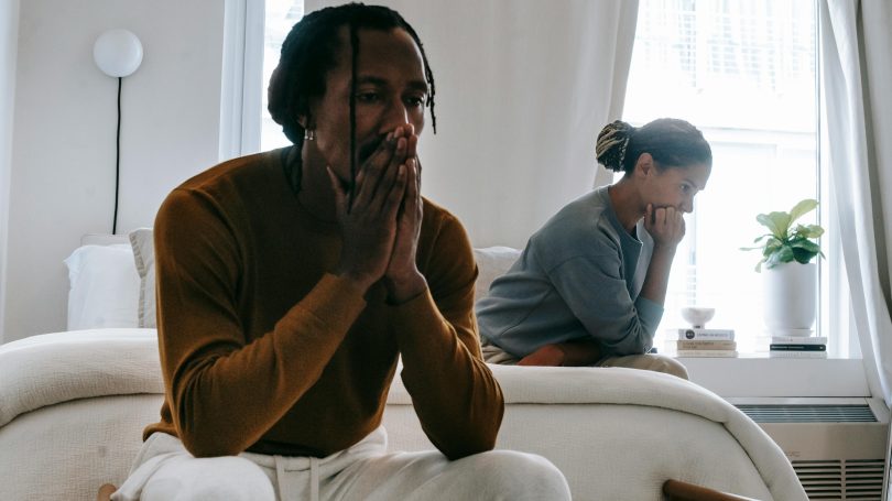 Man and woman sitting apart in a room, both appearing stressed and deep in thought, suggesting emotional tension or difficult conversation.