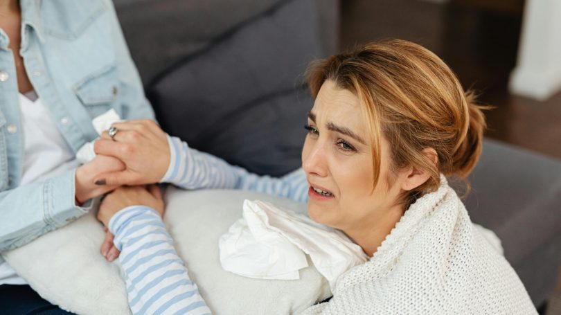 Grieving woman comforted by a friend on a couch, expressing emotional distress after miscarriage.