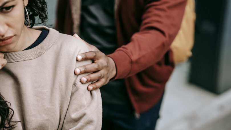 Close-up of a concerned woman being gently comforted by someone placing a supportive hand on her shoulder.