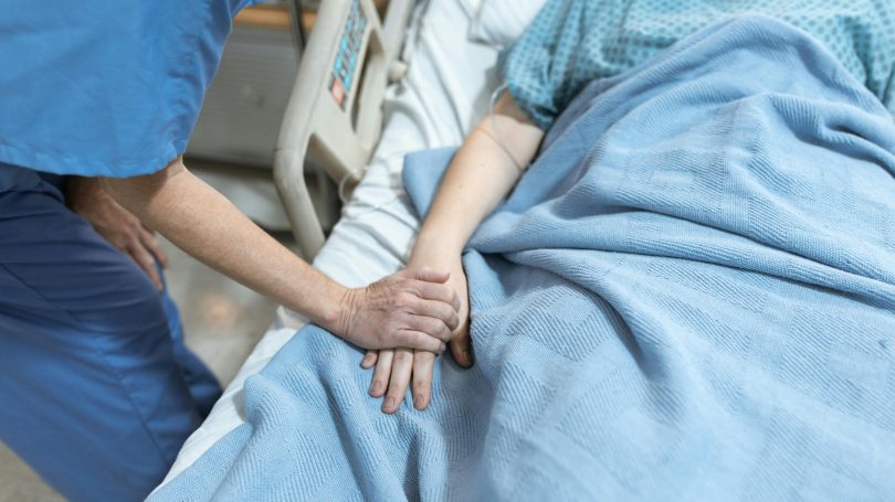 Healthcare worker holding the hand of a patient lying in a hospital bed, offering comfort and support during medical care.